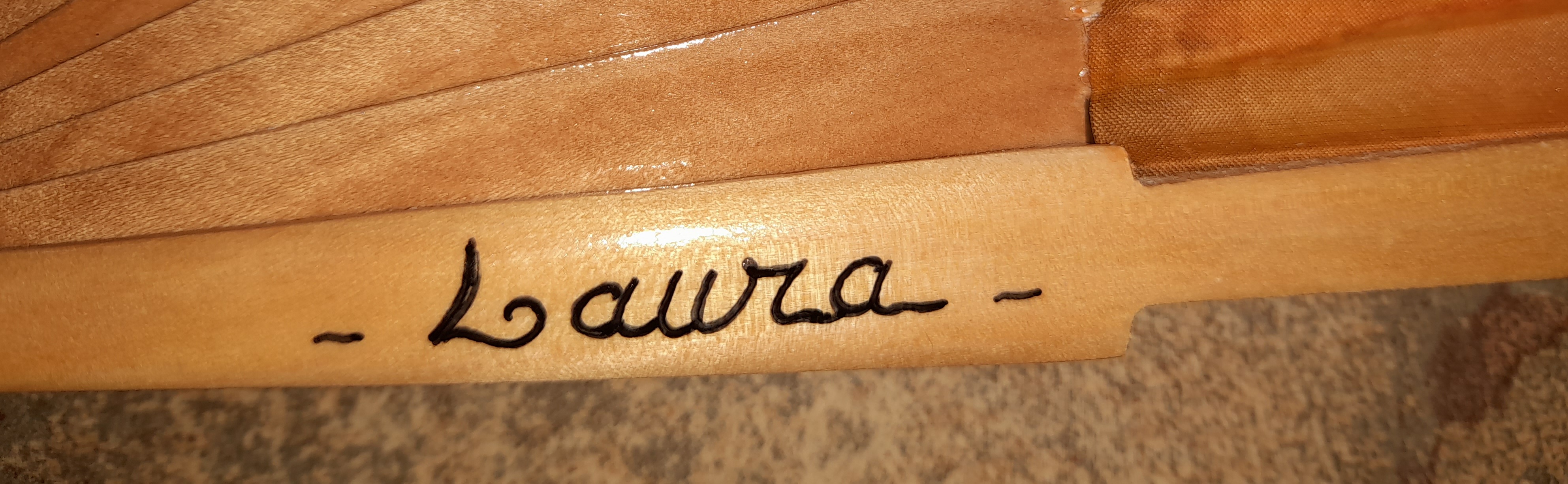 Signature artisanale peinte sur la branche d'un éventail en bois.
