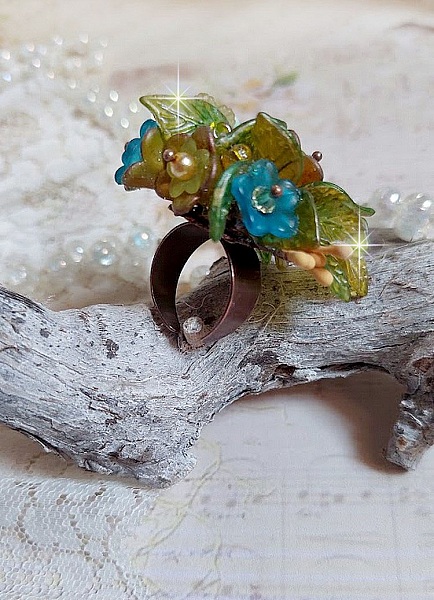 Bague C&eacute;zanne mont&eacute;e avec des petites fleurs lucites peintes &agrave; la main &agrave; laquelle s&rsquo;ajoute des feuilles, cristaux, perles, &eacute;tamines, grosses rocailles, perles nacr&eacute;es et m&eacute;tal sur une bague en Laiton