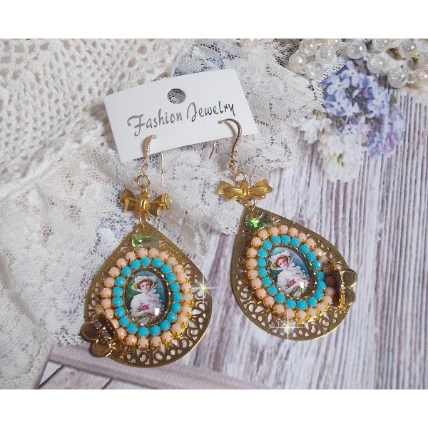 BO Mademoiselle Noellia avec des cabochons ovales repr&eacute;sentant une femme avec un chapeau et un n&oelig;ud blanc &agrave; laquelle s&rsquo;ajoute des cristaux, cha&icirc;nes strass P&ecirc;che et Turquoise sur crochets en plaqu&eacute; Or