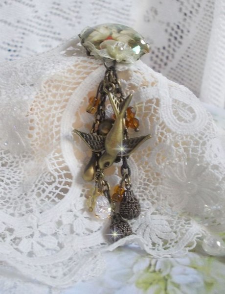 Broche Colombes aux plumages blancs avec des breloques filigran&eacute;es gouttes et lisses, perles rondes et n&oelig;ud en cristal, ruban organza cr&egrave;me, pendentif plaqu&eacute; or avec un zircon sur une broche en m&eacute;tal