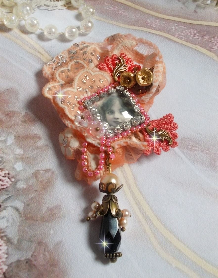 Rustic Rose Brosche mit einem Cabochon, der ein lächelndes Mädchen darstellt, orangefarbener Strass- und Rosenspitze, Kristallen, Glasperlen und verschiedenen Accessoires.