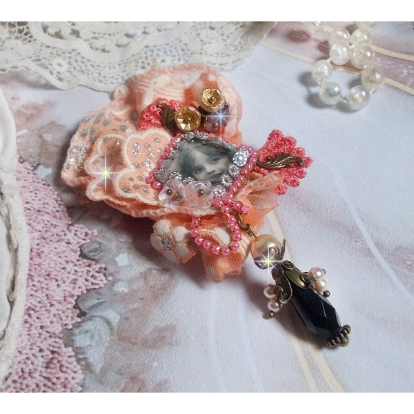 Rustic Rose Brosche mit einem Cabochon, der ein l&auml;chelndes M&auml;dchen darstellt, orangefarbener Strass- und Rosenspitze, Kristallen, Glasperlen und verschiedenen Accessoires.