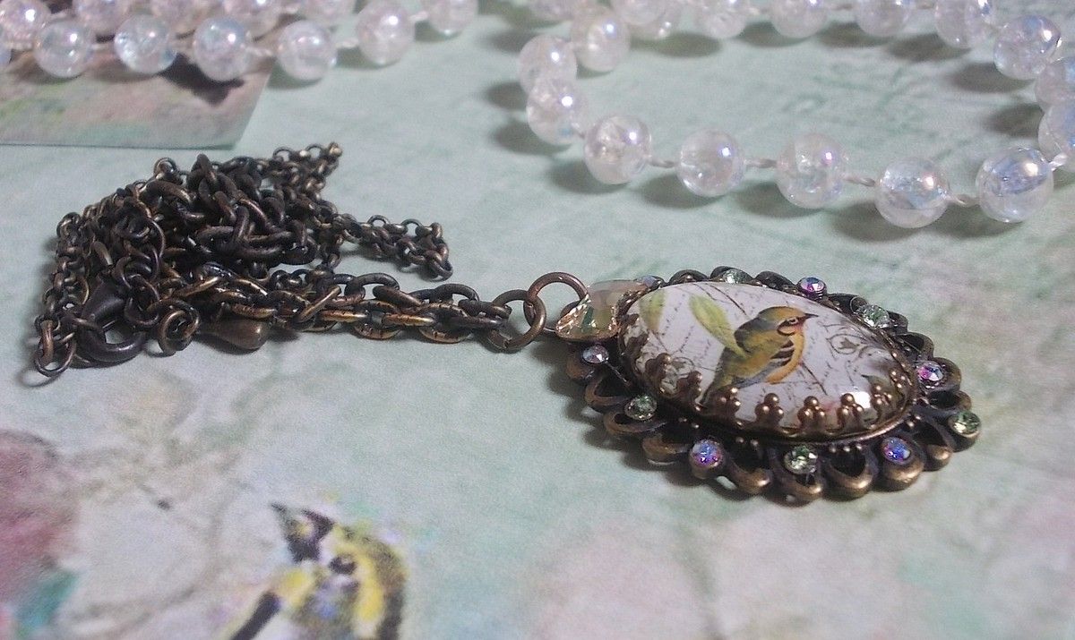 Gartenvogel-Halskette mit einem Lupen-Cabochon und Kristallen auf bronzefarbenen Accessoires.
