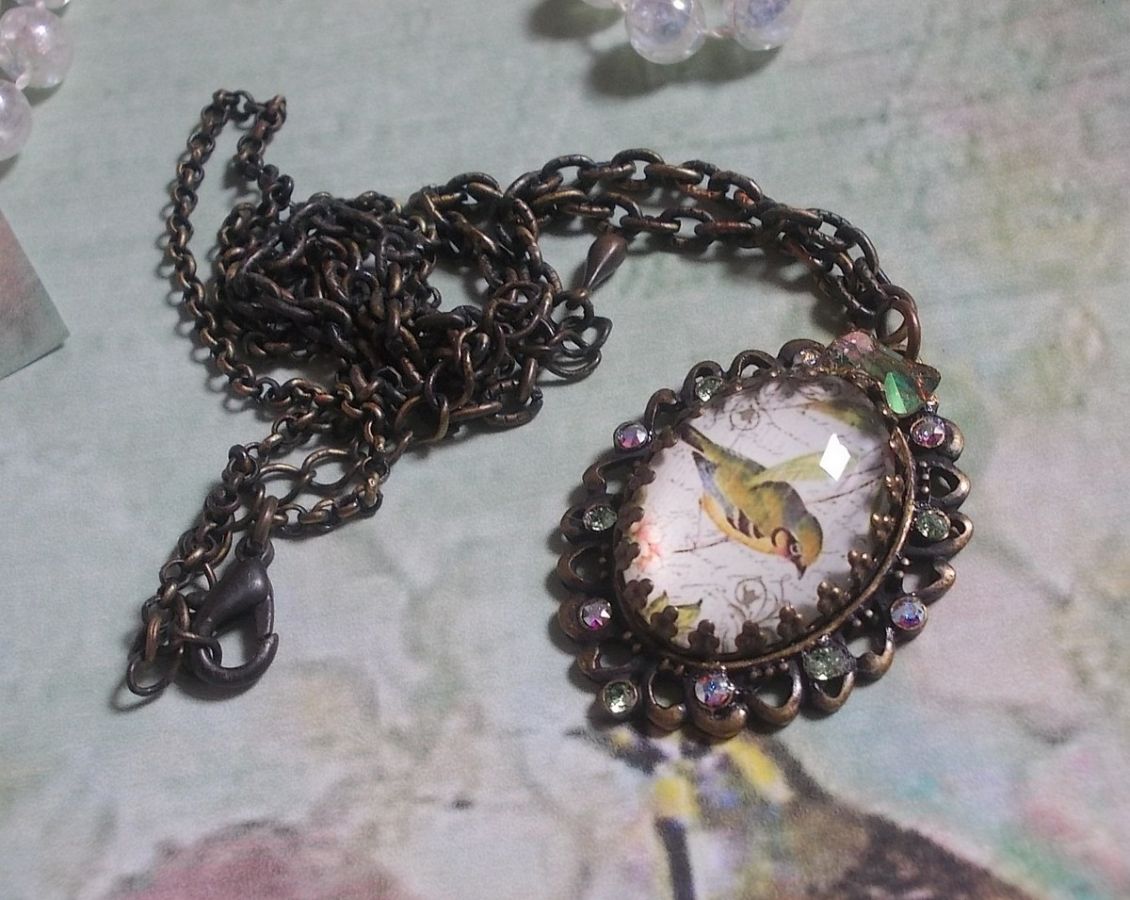 Gartenvogel-Halskette mit einem Lupen-Cabochon und Kristallen auf bronzefarbenen Accessoires.