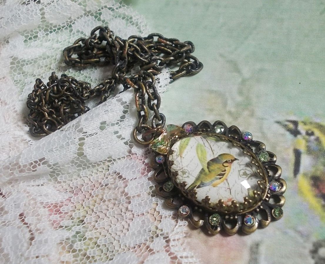 Gartenvogel-Halskette mit einem Lupen-Cabochon und Kristallen auf bronzefarbenen Accessoires.