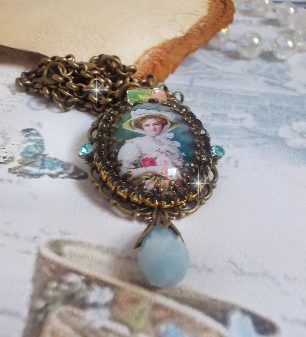 Pendentif Douce Dame créé avec un cabochon représentant une femme au chapeau blanc orné de cristaux, des accessoires de couleur Bronze et un jade teinté bleu 