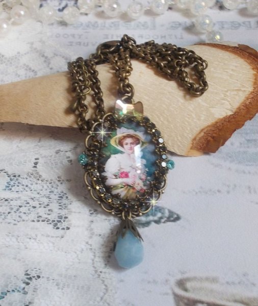 Pendentif Douce Dame cr&eacute;&eacute; avec un cabochon repr&eacute;sentant une femme au chapeau blanc orn&eacute; de cristaux, des accessoires de couleur Bronze et un jade teint&eacute; bleu 