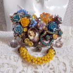 Broche Eclats Pétillants d’inspiration Baroque, ornée de fleurs en résine autour d’un cabochon strassés et perlés sur estampes, cristaux, breloques, perle cloisonnée, perles jaunes en verre et roses. 